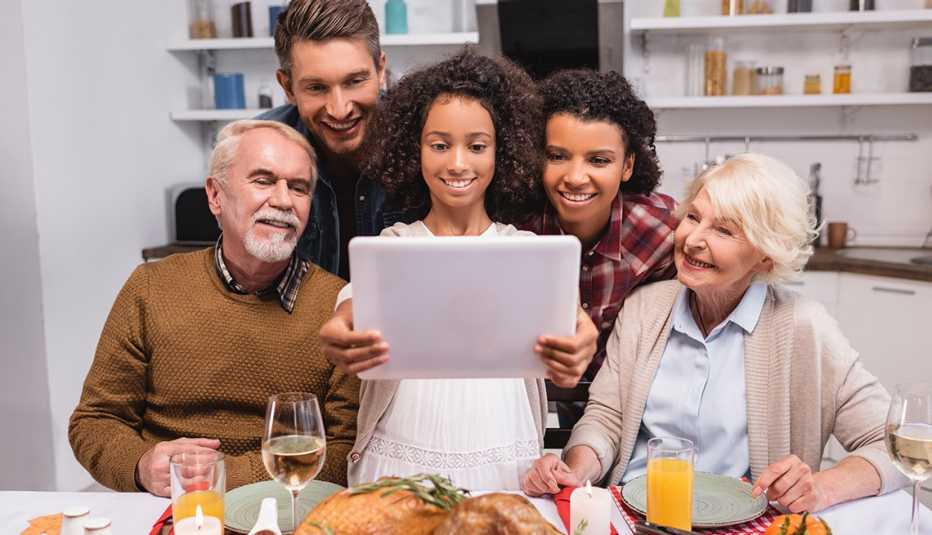 Una familia de cinco personas sosteniendo una tableta en la mesa de la cena conversando con miembros de la familia.