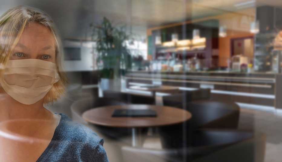 Una mujer usando una mascarilla mira un restaurante vacío a través de un cristal