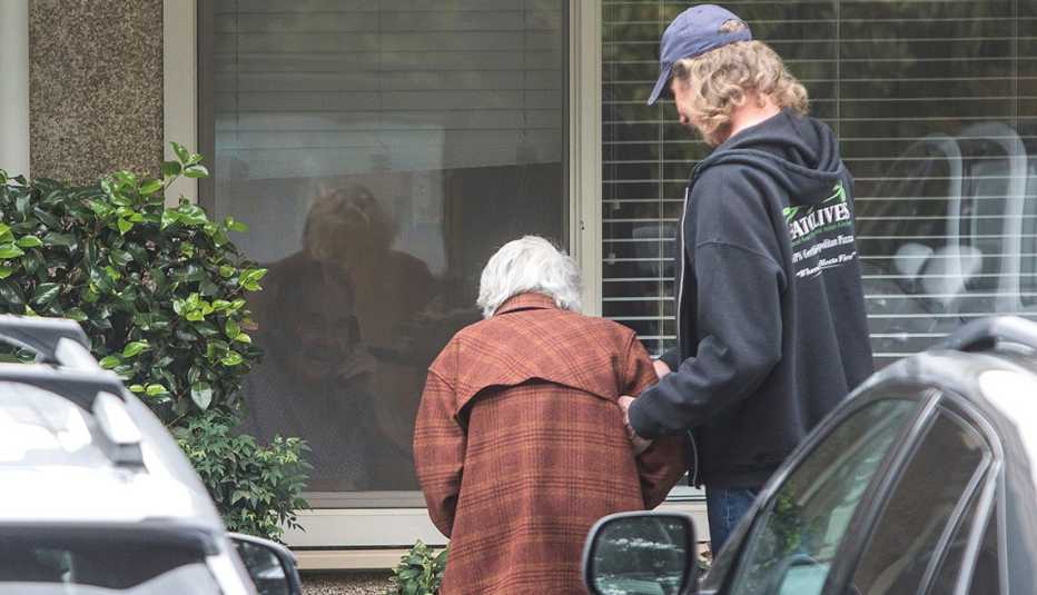 Un hombre ayuda a su mamá a ver a su papá a través de una ventana