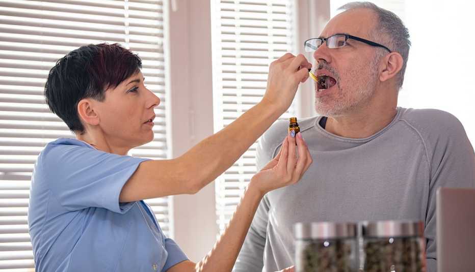 Enfermera pone unas gotas de aceite de marihuana en la boca de un hombre para aliviar el dolor