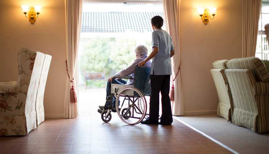 Una enfermera lleva un residente de un hogar de ancianos en silla de ruedas