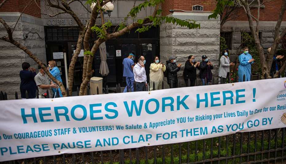 Trabajadores usando equipo de protección afuera de un hogar de ancianos  con un cartel que dice los héroes trabajan aquí