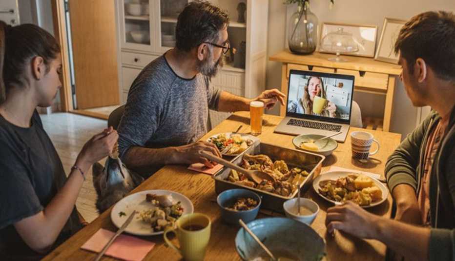 Familia sentada a la mesa cenando mientras conversan con una persona a través de una videollamada