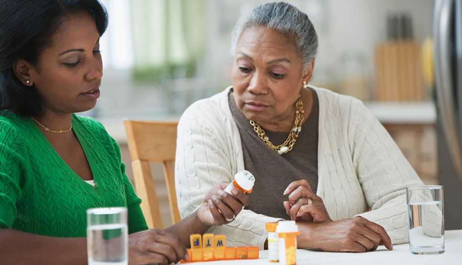 Una hija junto a su madre mirando frascos de medicamentos recetados. 