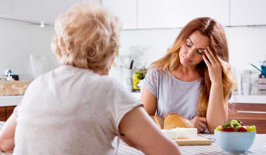 Mujer preocupada sentada en la mesa de la cocina y hablando con su madre mayor sobre los problemas.