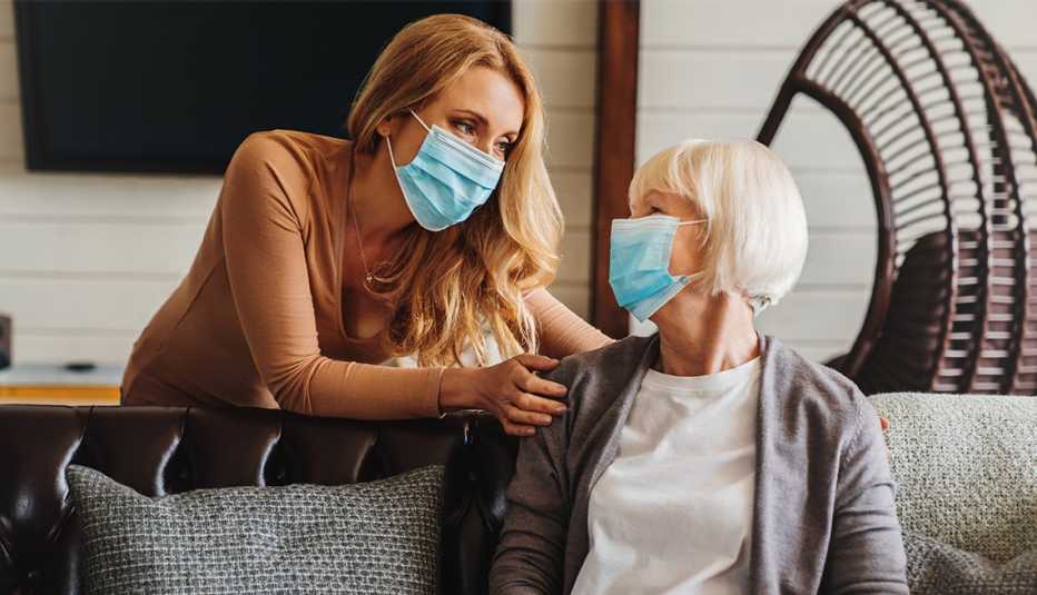 Un mujer con máscara médica es visitada por otra mujer.