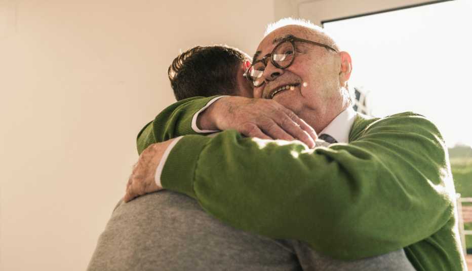 Un padre mayor abrazando a su hijo que lo visita en un hogar de ancianos.