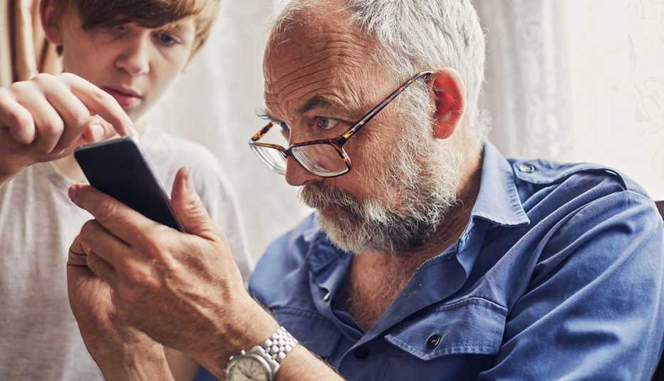 Un adolescente ayuda a su abuelo a usar un teléfono inteligente.
