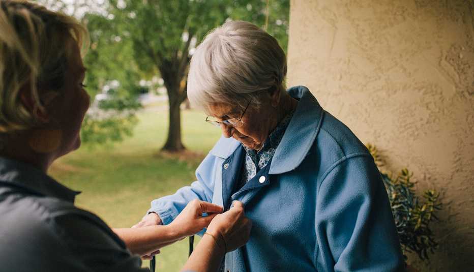 Una cuidadora ayuda a una mujer mayor con los botones de su camisa.