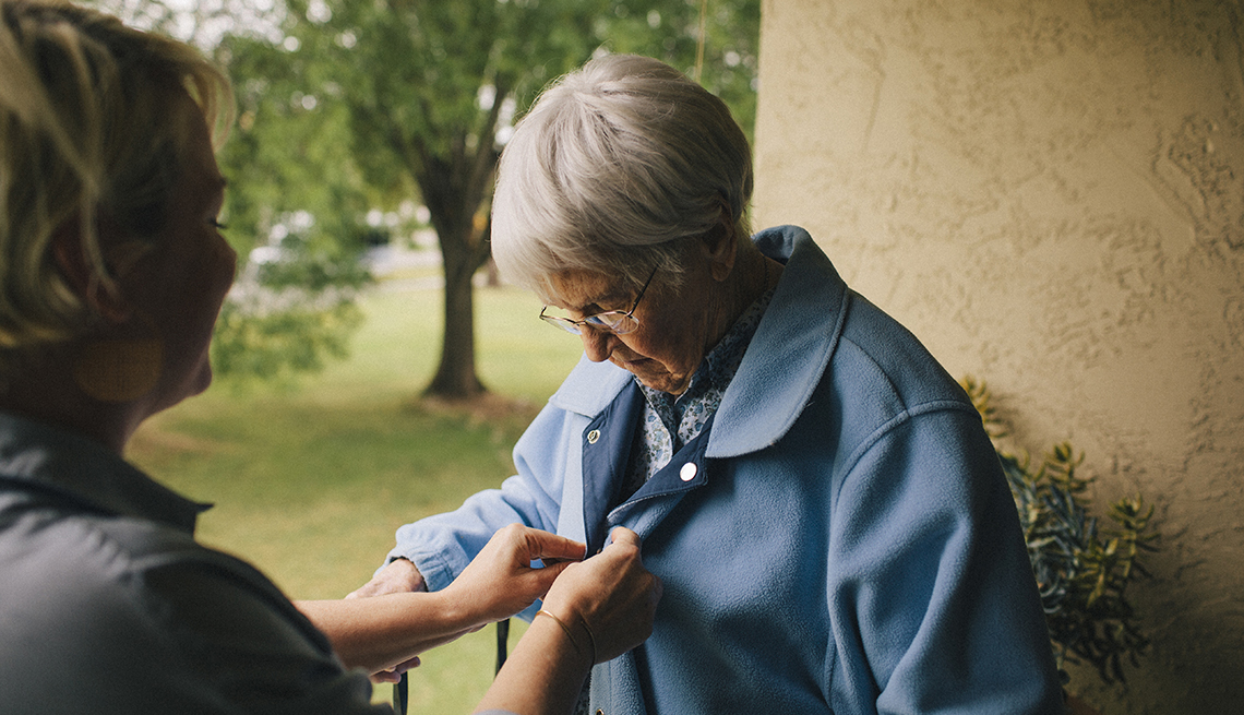 Una cuidadora ayuda a una mujer mayor con los botones de su camisa.