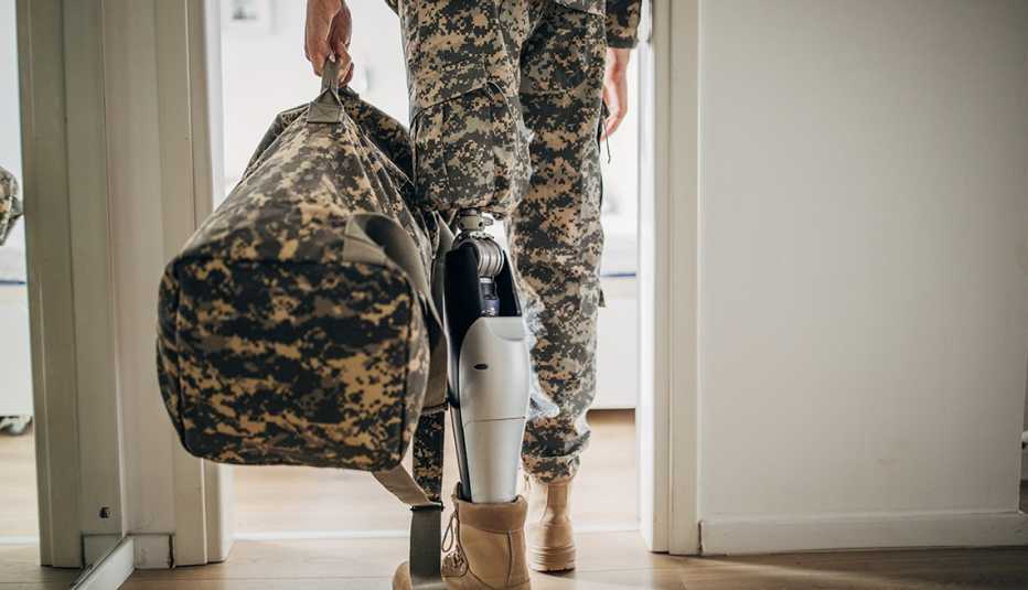 Un hombre con uniforme militar con una pierna amputada caminando por la puerta de una casa.