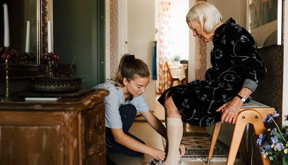 Una cuidadora ayuda a una mujer mayor a ponerse los zapatos.