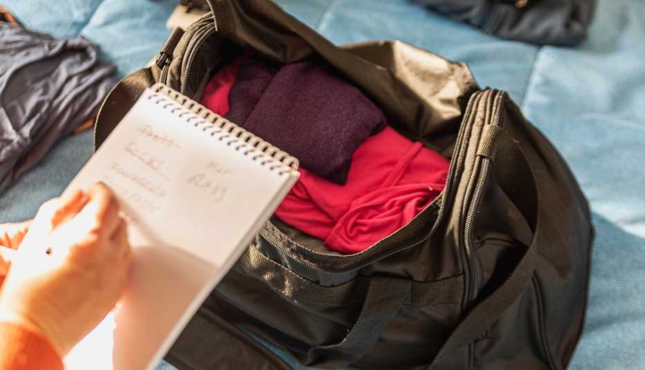 Un bolso de emergencia con ropa y las manos de una persona escribiendo un listado en una libreta.