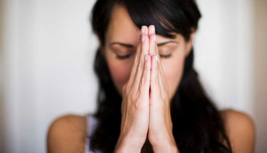 Mujer de pelo negro con las manos en posición de meditación o rezo.