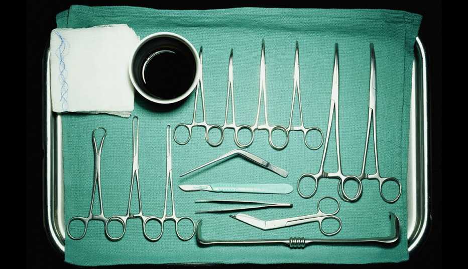 Instrumentos quirúrgicos colocados en bandeja de metal con un paño verde. 