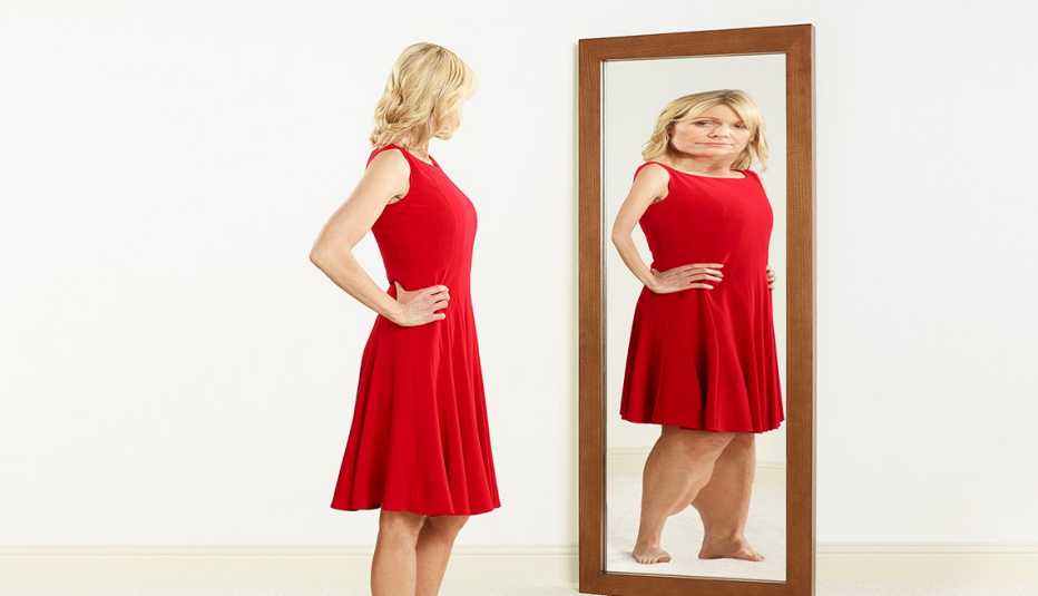 Mujer vestida de rojo ve el reflejo de su imagen deformada en un espejo.