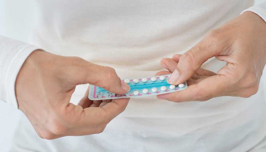 Mujer sostiene con sus manos una tirilla de tabletas anticonceptivas.