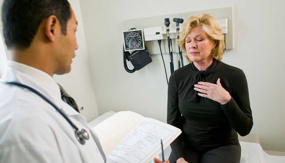 Una mujer, se lleva la mano al pecho en señal de queja mientra habla con su doctor