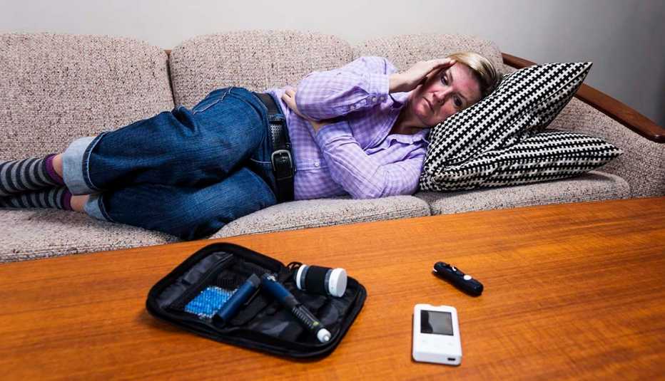 Mujer acostada en un sofá y un glucómetro sobre una mesa