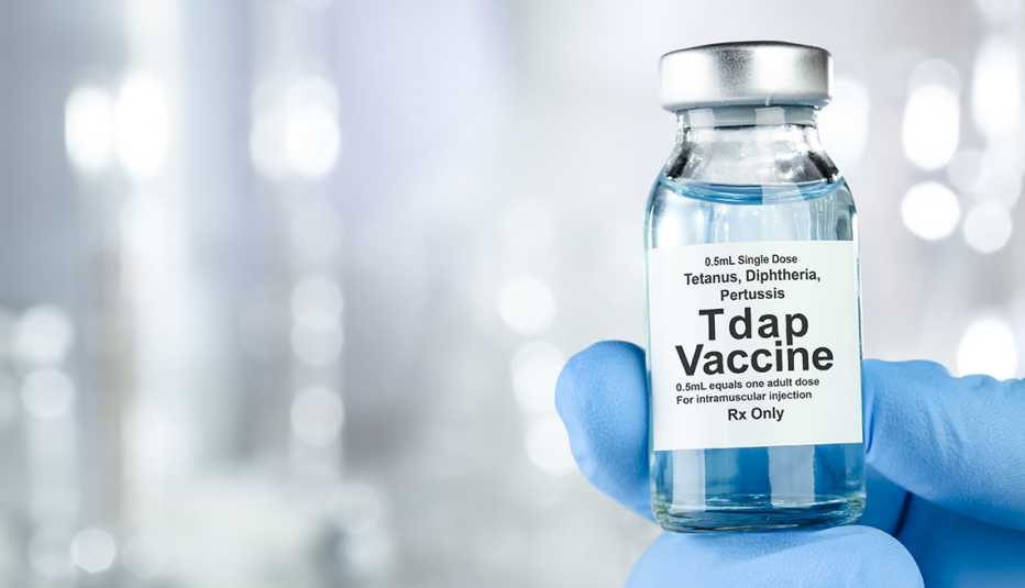 Una mano con un guante azul sostiene un frasco de la vacuna Tdap