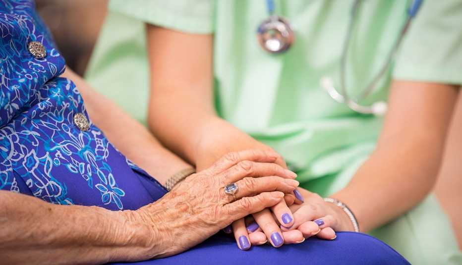 Personal médico sosteniendo las manos de una mujer mayor