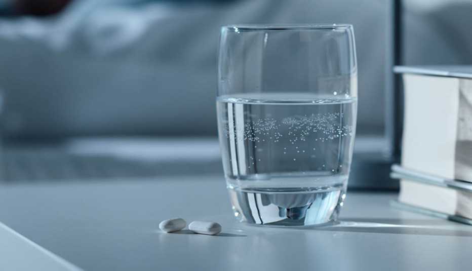 Vaso con agua y pastillas sobre una mesa de noche