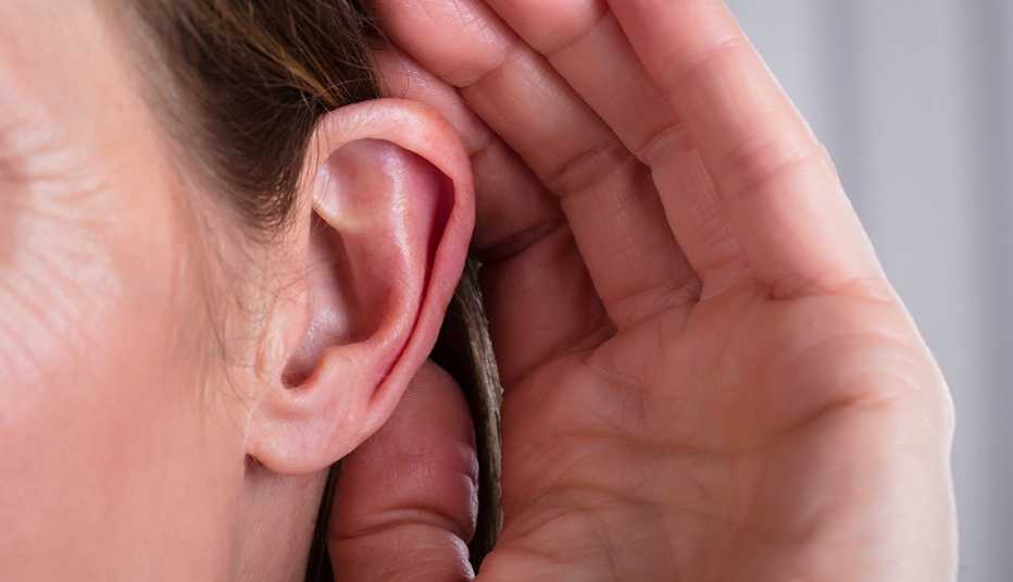 Una mujer lleva su mano a la oreja para escuchar mejor