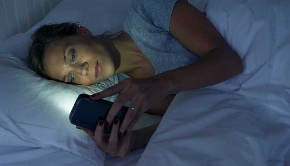 Una mujer acostada en su cama usando su teléfono