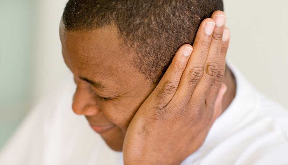 Un hombre con dolor de oído se cubre la oreja con la mano