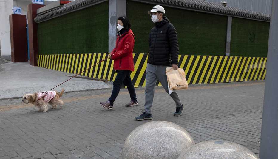 Una pareja usando mascarillas camina su perro