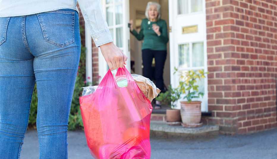 Una mujer le lleva un bolso de alimentos a una mujer mayor que la recibe en su casa