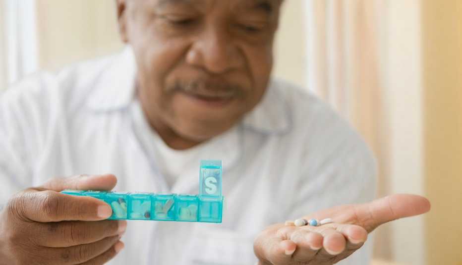 Un hombre sostiene una caja plástica con sus pastillas diarias