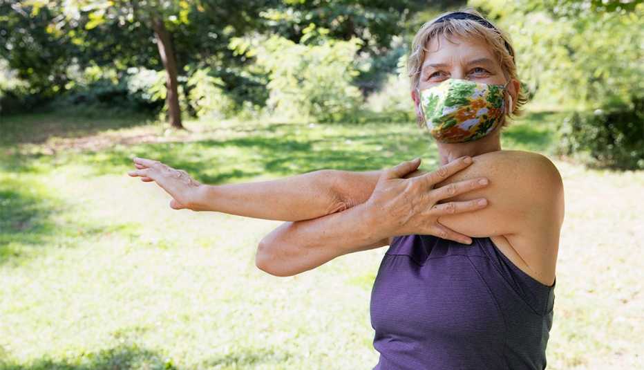 Una mujer hace ejercicio afuera en un parque mientras usa una mascarilla