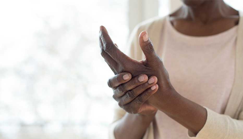 Una mujer se masajea sus manos para aliviar el dolor de la artritis