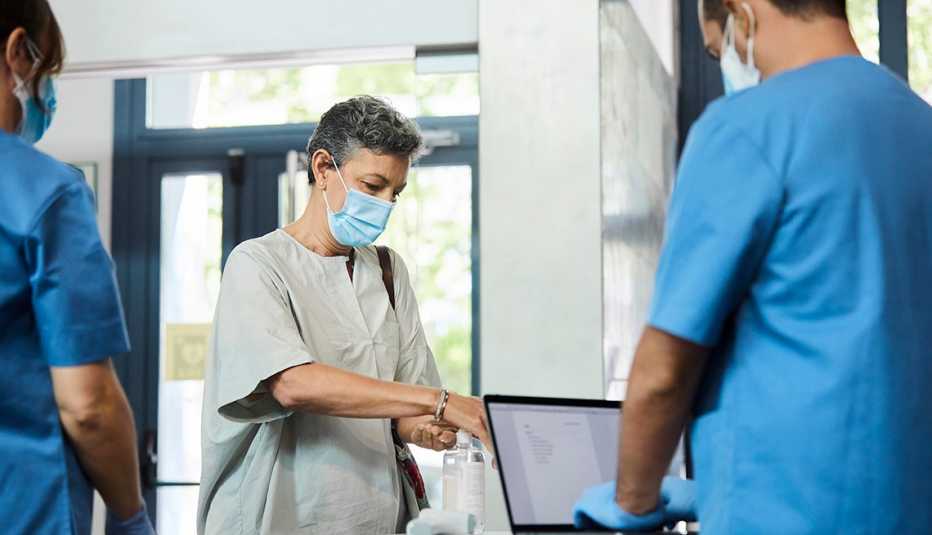 Una mujer se pone desinfectante en las manos mientras dos enfermeros la observan