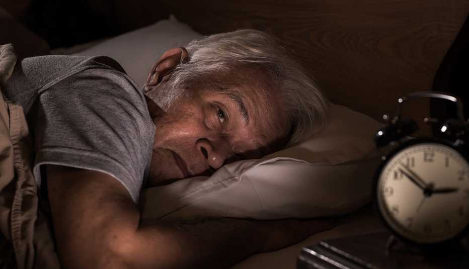 Un hombre mayor acostado en su cama y sin poder dormir
