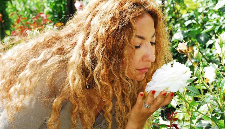 Una mujer se dobla para oler una flor en su jardín