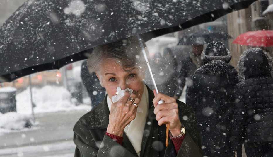 Una mujer limpia su nariz con un pañuelo mientras camina con una sombrilla bajo la nieve