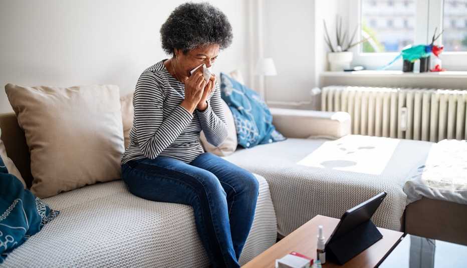 Una mujer se limpia la nariz sentada en el sofá de su hogar