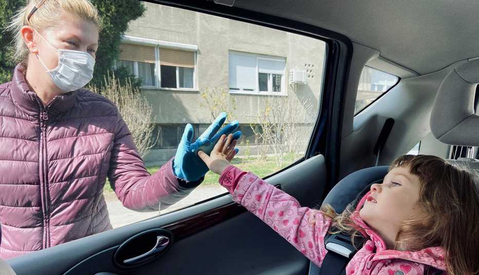 Una mujer toca la ventana de un auto desde afuera y en el interior una niñita hace lo mismo