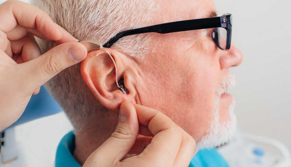 Un médico pone un pequeño audífono inteligente en el oído de un hombre