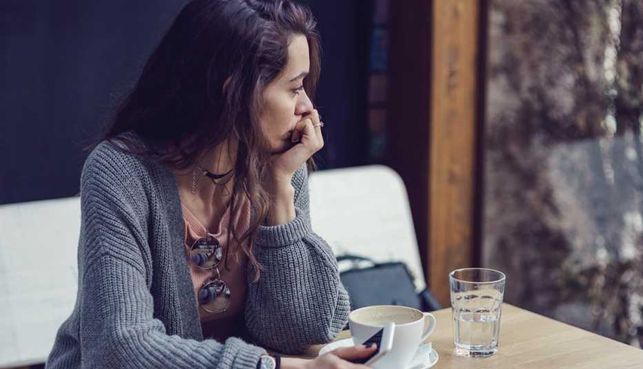 Una mujer mira pensativa mientras sostiene una taza de café