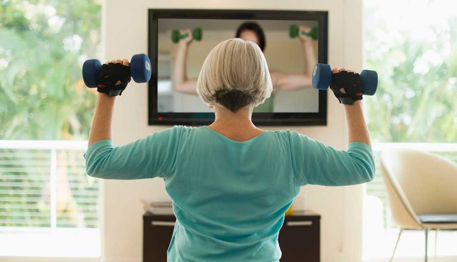 Una mujer hace ejercicios en la sala de su casa mientras ve un video en la TV