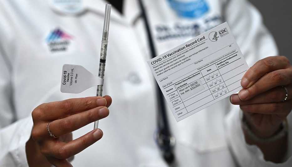 Un médico sostiene una jeringa en una mano y una tarjeta de vacunación contra la COVID-19 en la otra