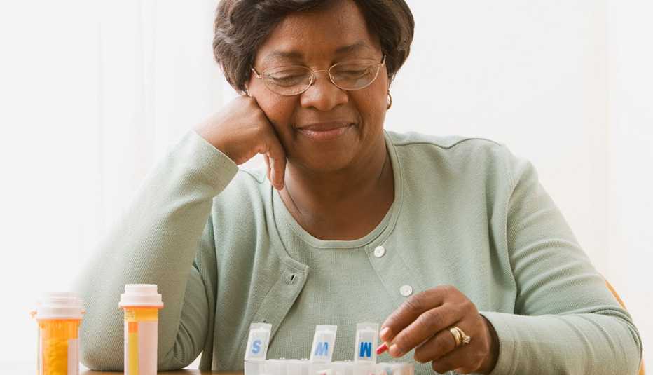 Mujer poniendo sus medicamentos recetados en un pastillero