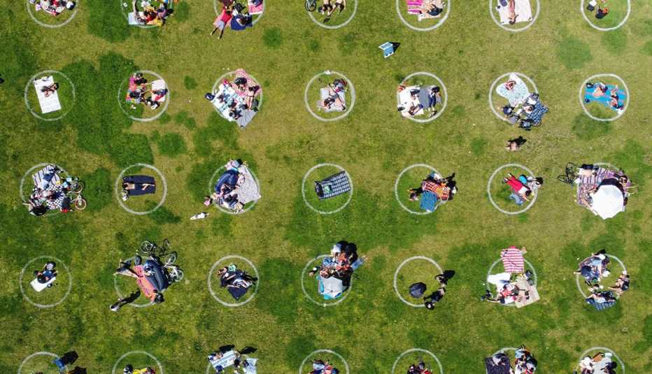 Foto aérea de personas en un parque cubierto de hierba dentro de círculos de distanciamiento social pintados sobre el césped