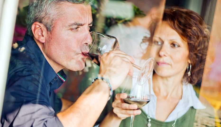 Un hombre maduro toma una copa de vino mientras una mujer lo observa