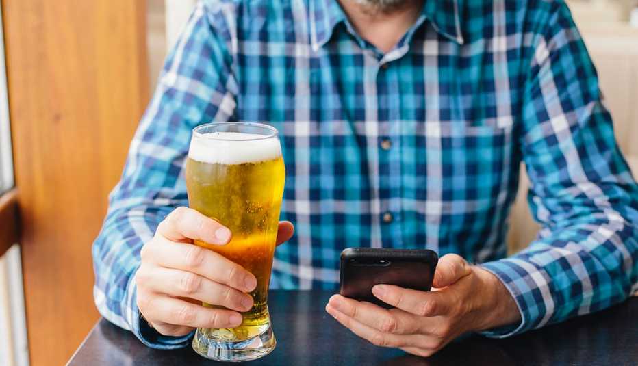 Un hombre con una cerveza en la mano y su celular en la otra