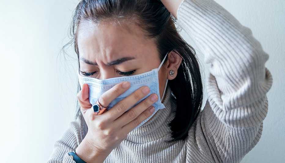Una mujer usando mascarilla mientras estornuda y se aguanta la cabeza