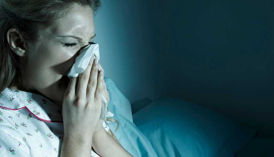 Una mujer se cubre la boca y nariz con un pañuelo mientras estornuda